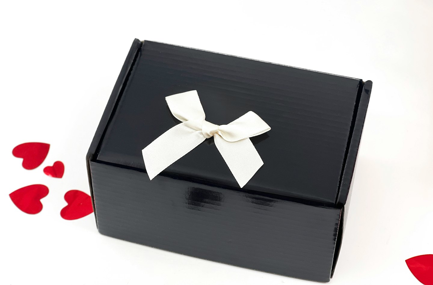 Black gift box with a cream ribbon surrounded by red hearts.